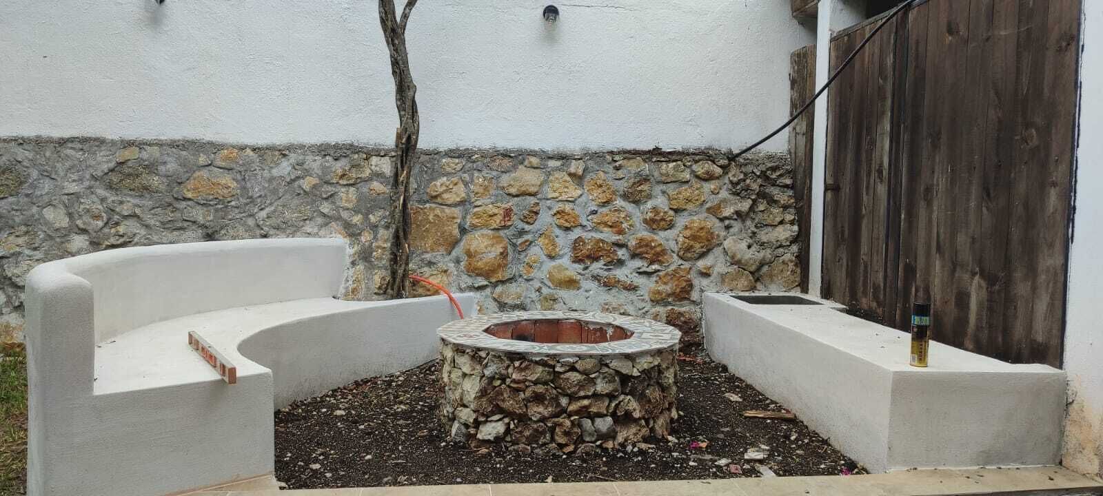 Una chimenea de piedra rodeada de zonas de estar con asientos de concreto blanco.
