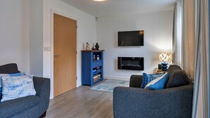 Ett modernt vardagsrum med en platt-TV, en blå möbel för underhållningssystemet och två grå soffor.