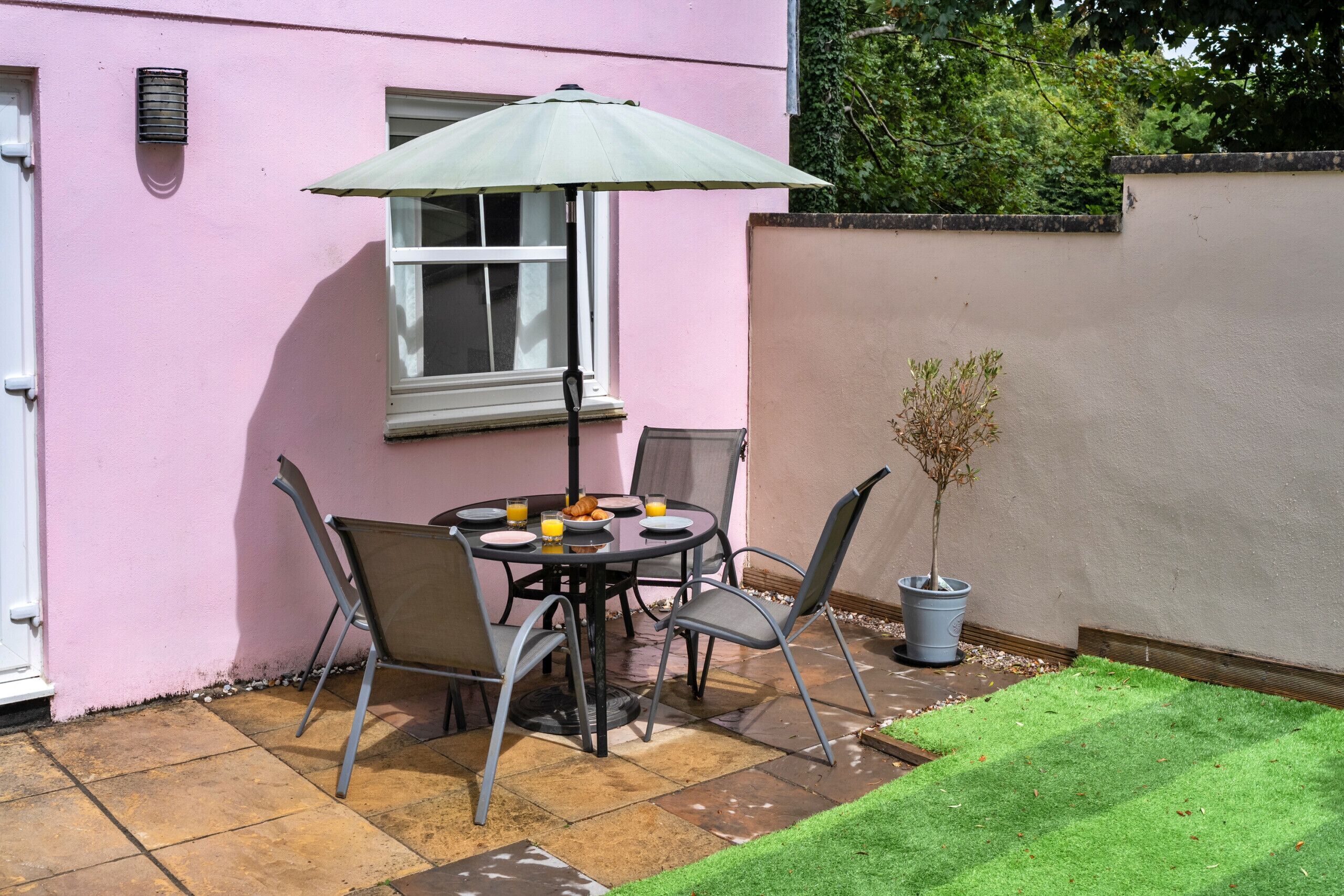 An outdoor patio with a table, chairs, and a potted plant.
