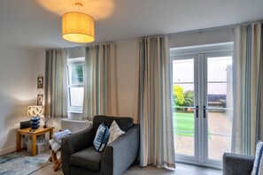 En stue med en sofa, en lampe, et lille bord og udsigt til en have gennem en skydedør.