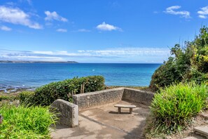 A coastal bench area with a view of the sea, surrounded by greenery. - Marshmallow House (Duporth)