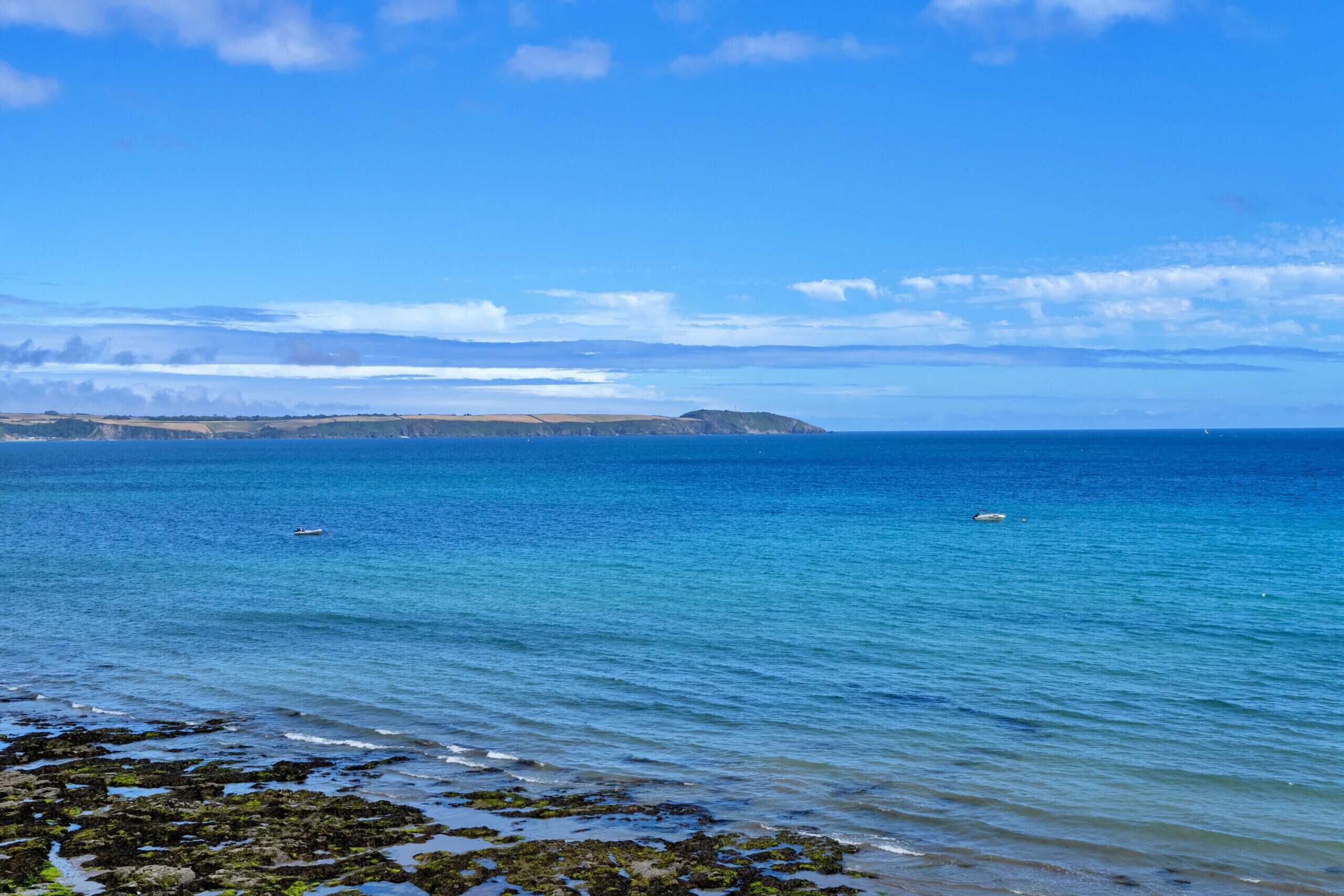 A coastal landscape with clear blue waters, rocky shoreline, and distant landforms.