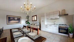 A dining area with a chandelier, a painting, and a view of the kitchen.