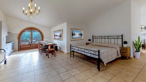 A bedroom with a bed, bedside tables, a nightstand, a potted plant, a window with a view, and a chandelier.