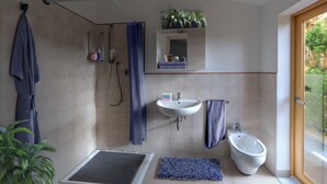 A modern bathroom with a shower, sink, bidet, and a window with a view.