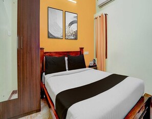 A bedroom with a wooden bed, two framed pictures on the wall, a nightstand, and a window with curtains. - Deluxe Ethal Residency (Hosur)