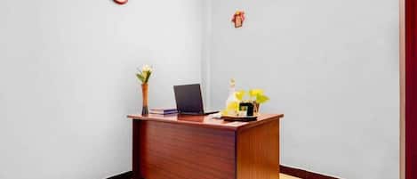 A reception desk with a laptop, a vase with flowers, and a clock on the wall.