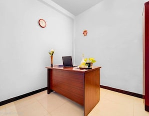 Un mostrador de recepción con una computadora portátil, un florero con flores y un reloj en la pared.