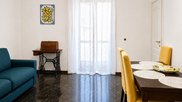 Een woonkamer met een bank, een tafel met een houten kist, een naaimachine en een eetgedeelte met stoelen en een tafel.