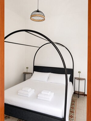 A bed with a black metal frame and white bedding, two bedside tables with lamps, and a hanging light fixture. - Charming Retreat near Historic Landmarks (Modica)