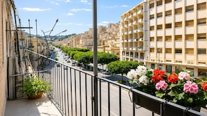 A balcony with a view of a city street, a row of parked cars, and a building with multiple balconies.