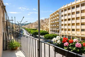 A balcony with a view of a city street, a row of parked cars, and a building with multiple balconies. - Charming Retreat near Historic Landmarks (Modica)