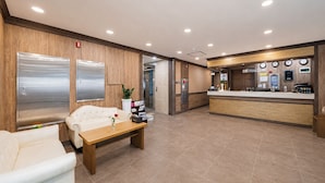 Un vestíbulo de hotel con un mostrador de recepción, una zona de espera con un sofá y una mesa de centro, y un mostrador de recepción con un reloj y una planta.