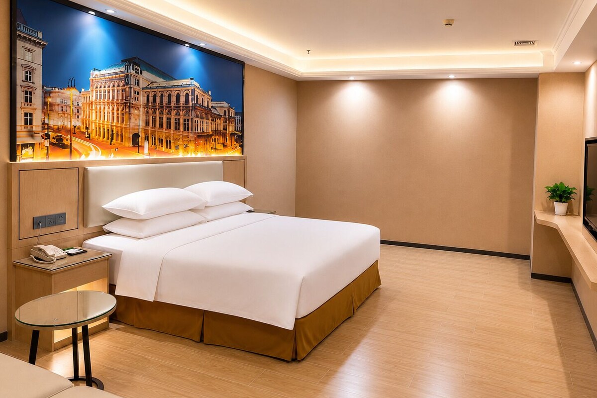 Ein Hotelzimmer mit Bett, Nachttisch, Lampe und einem an der Wand befestigten Fernseher.