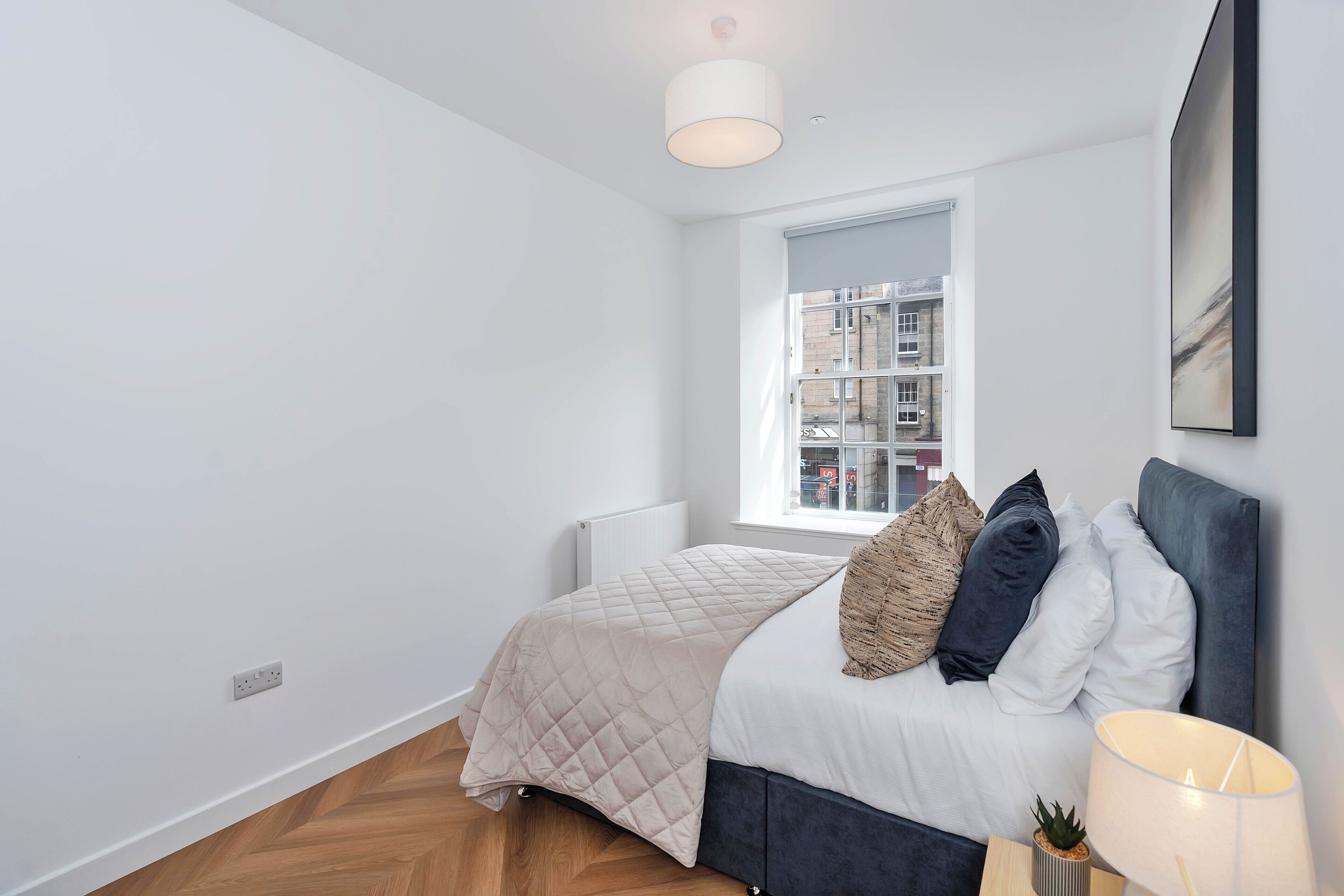 A modern bedroom with a bed, a window, a radiator, and a wall-mounted lamp.