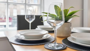 Uma mesa de jantar com um vaso de planta, dois copos de vinho e pratos postos para uma refeição.