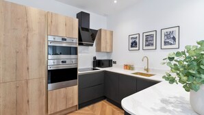 Uma cozinha moderna com eletrodomésticos embutidos, piso de madeira em padrão herringbone, bancada de mármore branco e pia com torneira dourada.