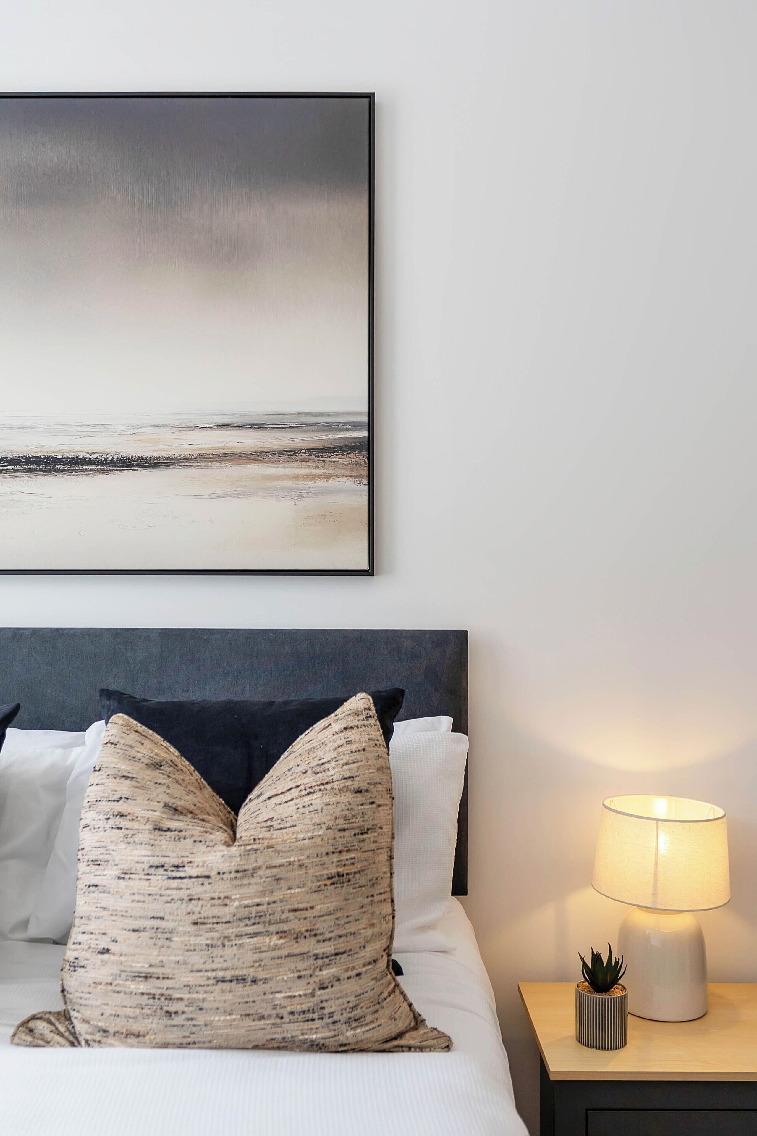A neatly made bed with a headboard, a bedside lamp, and a framed picture on the wall.