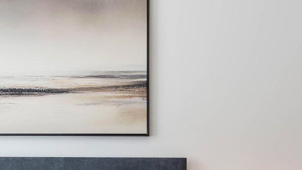 Uma cama bem arrumada com cabeceira, uma luminária de mesa e um quadro na parede.