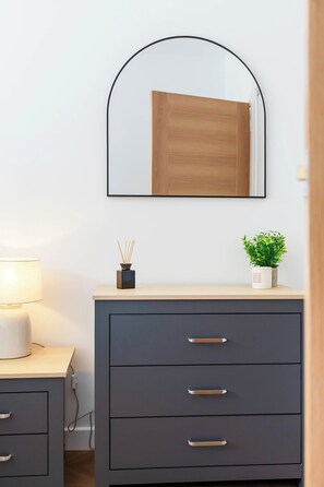 Ein modernes Zimmer mit einem Holzschrank, einem Spiegel, einer kleinen Topfpflanze und einer Lampe.