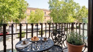 A balcony with a table set for two, a potted plant, and a view of the street and buildings. - ALL Savoia Station – Elegance, Relax & Comfort in the Heart of Bari (Bari)