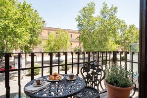 A balcony with a table set for two, a potted plant, and a view of the street and buildings. - ALL Savoia Station – Elegance, Relax & Comfort in the Heart of Bari (Bari)