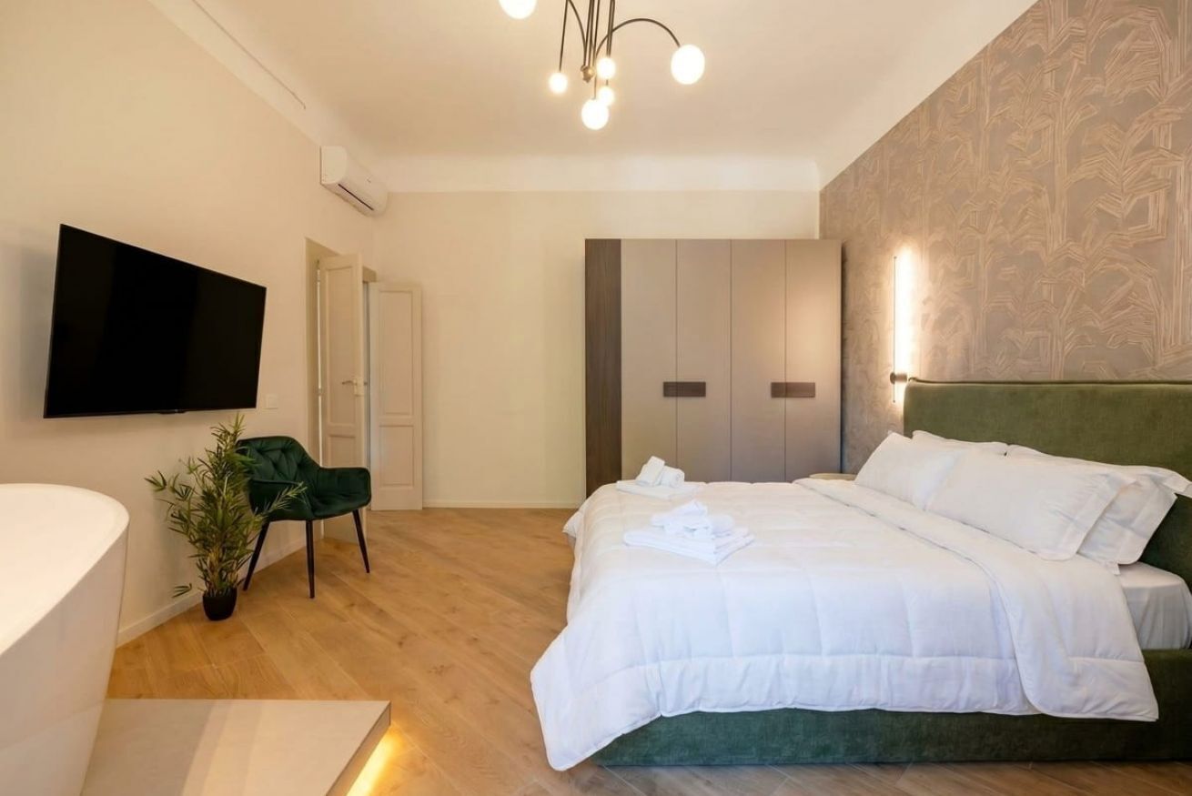 A modern hotel room with a bed, a TV, a green chair, and a plant.