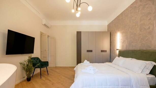 A modern hotel room with a bed, a TV, a green chair, and a plant. - ALL Savoia Station – Elegance, Relax & Comfort in the Heart of Bari (Bari)