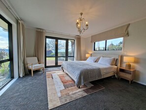Ein Schlafzimmer mit einem großen Bett, zwei Nachttischen, einer Chandelierleuchtre, Blick durch das Fenster und einem Sessel.