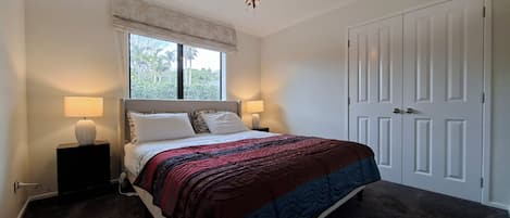 A bedroom with a bed, two bedside lamps, a window with a view, a chandelier, and a door.