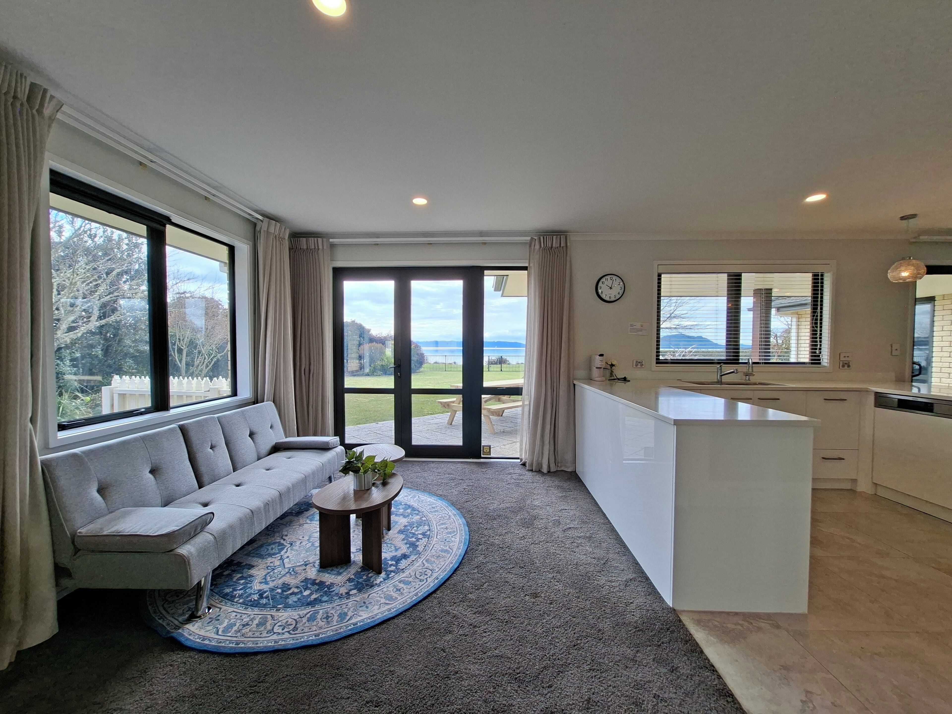 A modern living room with a sofa, a coffee table, and a view of the outdoors through a sliding glass door.