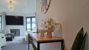 Ein modernes Wohnzimmer mit einem Holztisch, einer Wanduhr und einer Vase mit weißen Blumen.