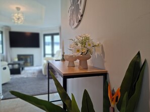 Ein modernes Wohnzimmer mit einem Holztisch, einer Wanduhr und einer Vase mit weißen Blumen.