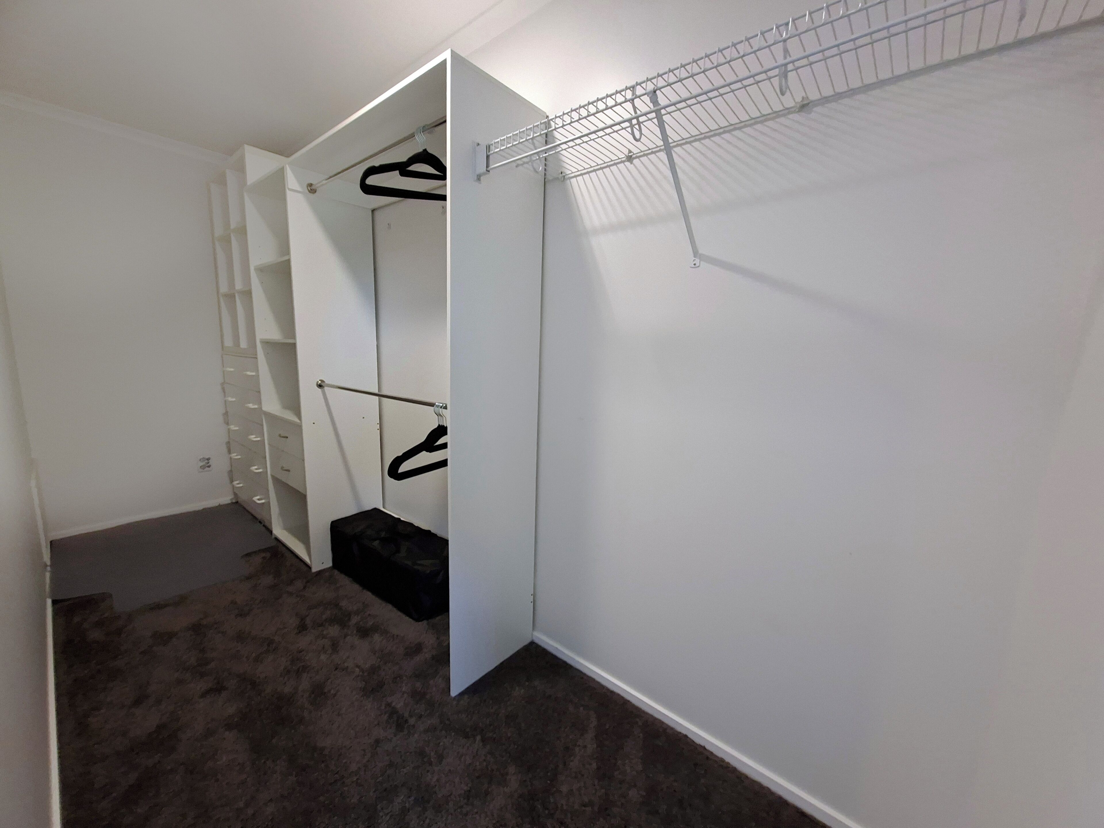 Ein begehbarer Kleiderschrank mit offenen Regalen, einer Kleiderstange und einem Schuhregal.