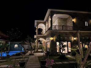 Un edificio de varios pisos con piscina, iluminación exterior y un jardín bien cuidado.