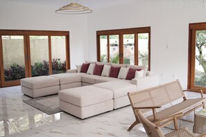 Una sala moderna con un sofá modular, un banco tejido y una mesa de centro de vidrio.