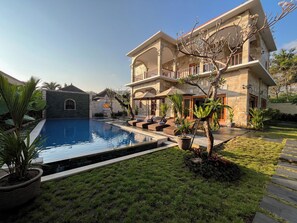 A two-story building with a swimming pool, outdoor seating, and a well-maintained garden.