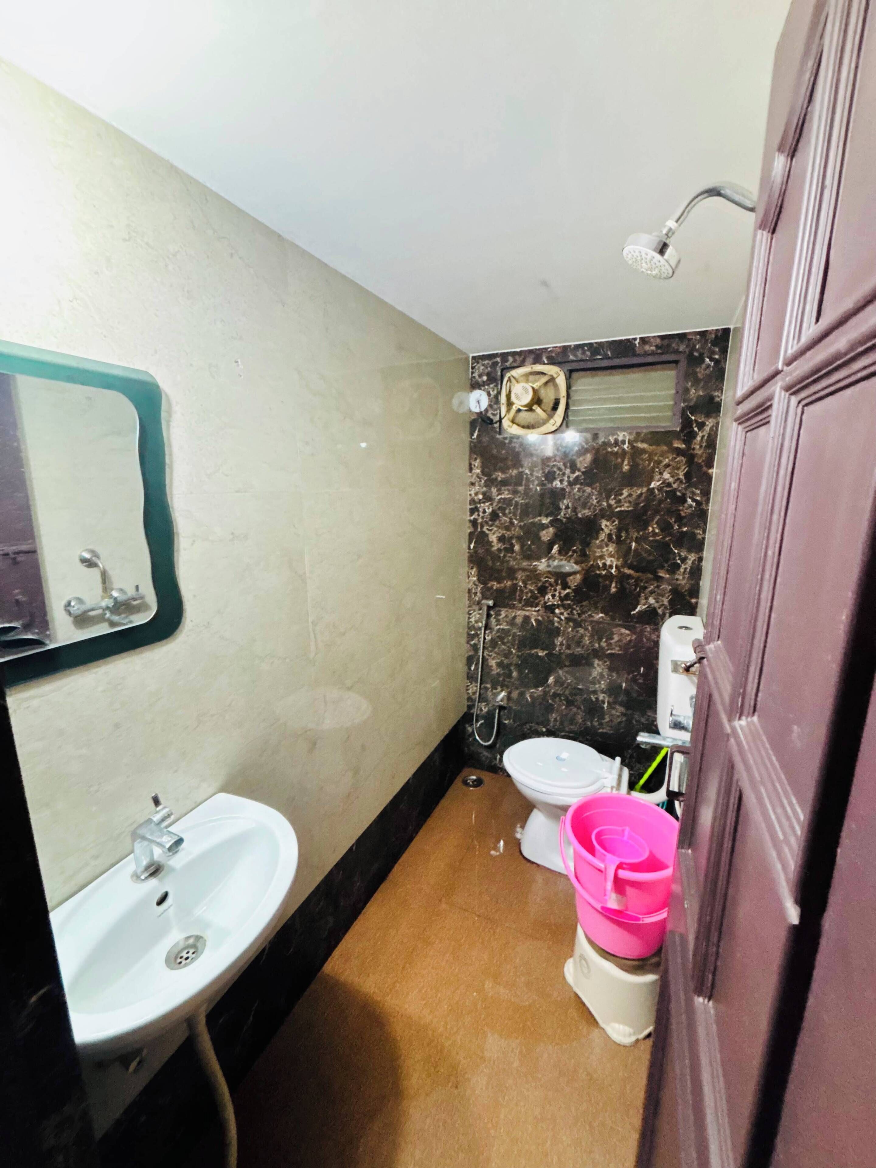 Casa de banho com lavatório, sanita, chuveiro e espelho.