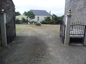A gated entrance to a property with a gravel driveway leading to a building with a tiled roof. - A townhouse in the countryside by the sea. 30 m². Small dogs are allowed. (Saint-Michel-Chef-Chef)