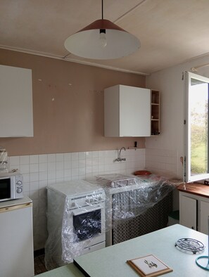 A kitchen with white cabinets, a microwave, and a sink covered in plastic. - A townhouse in the countryside by the sea. 30 m². Small dogs are allowed. (Saint-Michel-Chef-Chef)