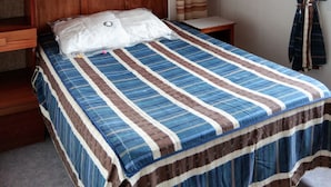 A bedroom with a wooden headboard, a bed with a striped bedspread, a bedside table, a hanging light fixture, a wall-mounted shelf, and a curtain.