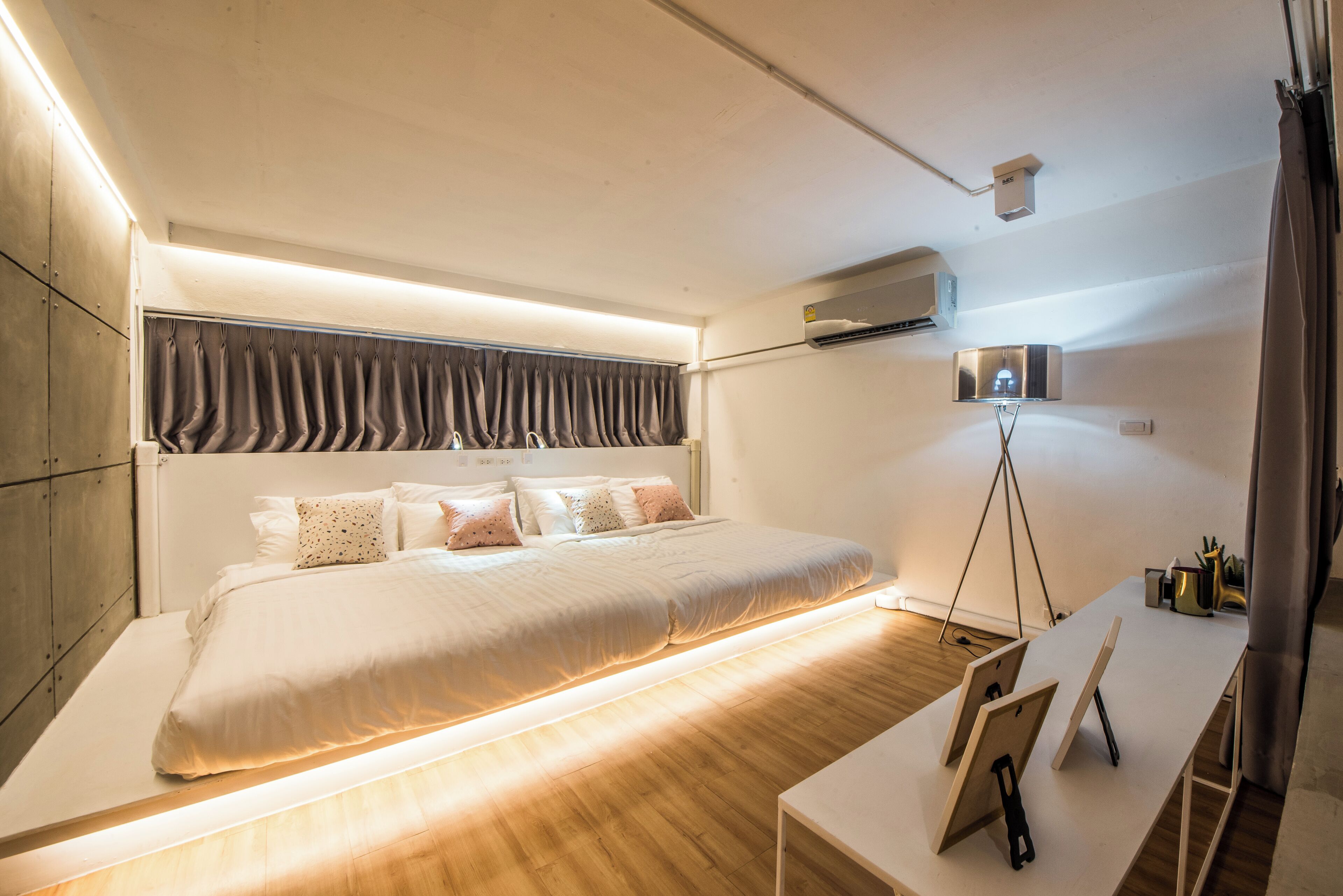 Een moderne slaapkamer met een groot bed, nachtkastjes, een airconditioning en een bureau met een lamp.