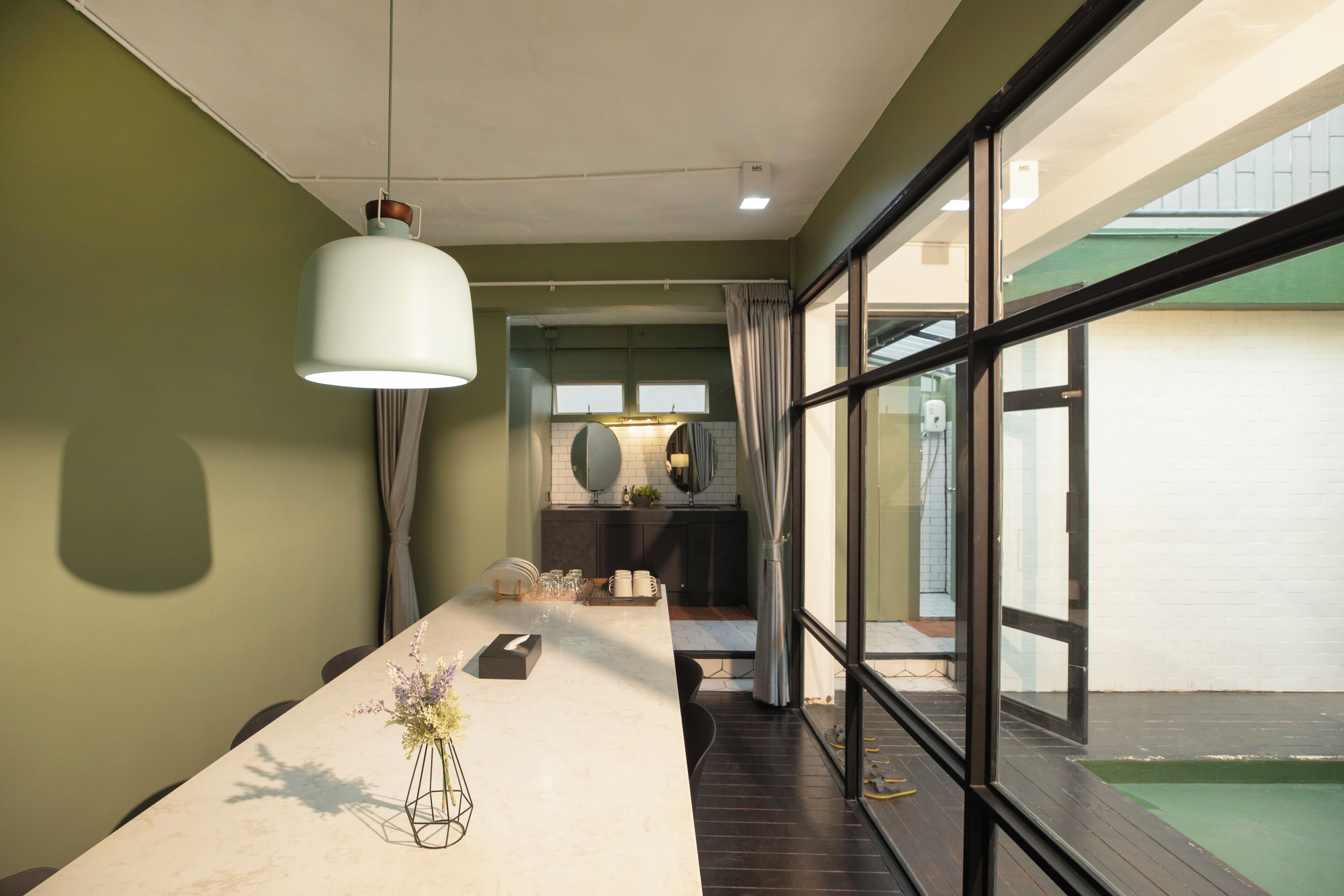 A modern interior with a long dining table, a hanging light fixture, and a view through large windows.