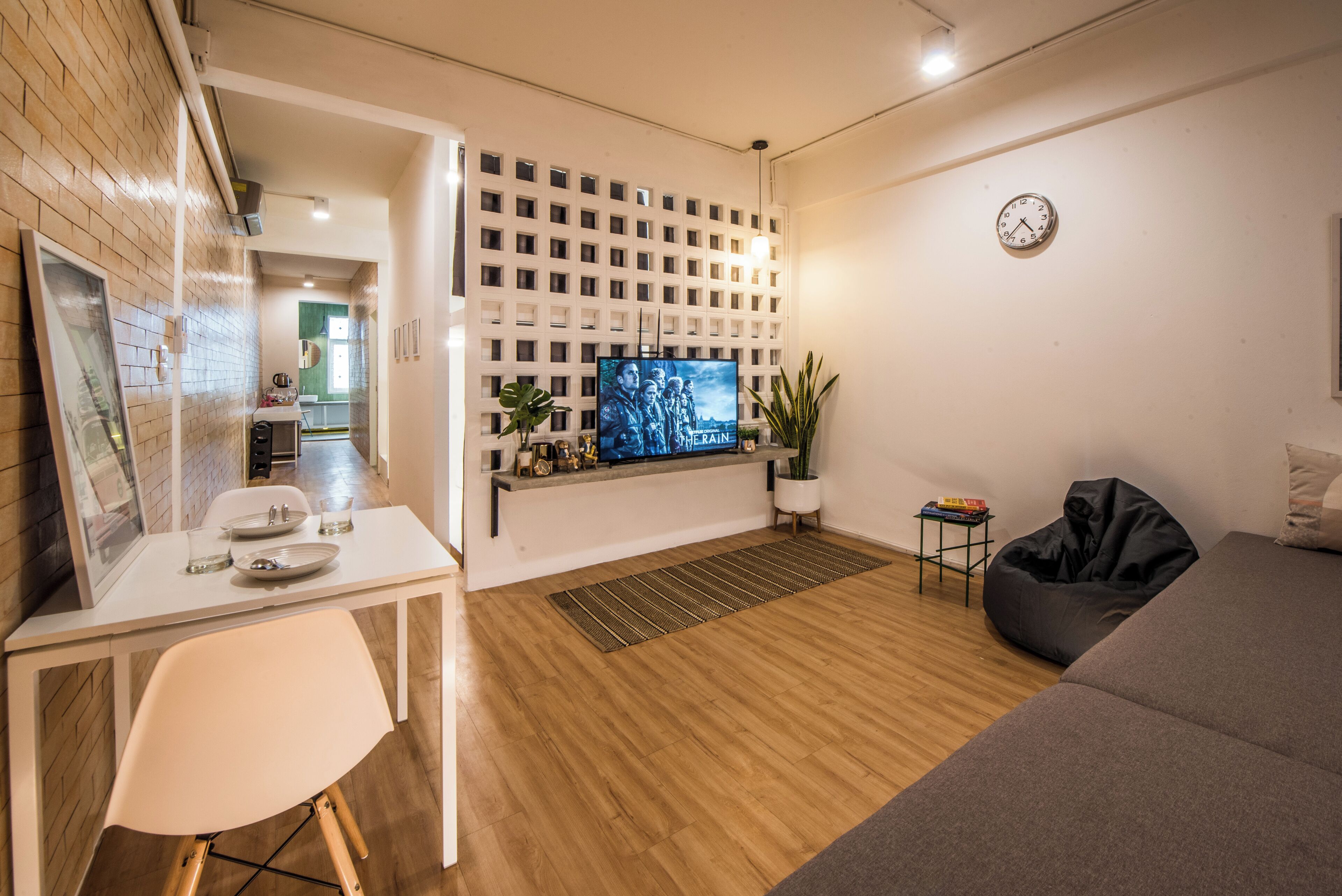 Een moderne woonkamer met een flatscreen televisie aan de muur, een eettafel met stoelen, een zwarte loungestoel en een bijzettafeltje met boeken.