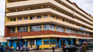 Un edificio de varios pisos con fachada plana, múltiples ventanas y un espacio comercial en la planta baja con diversas tiendas.