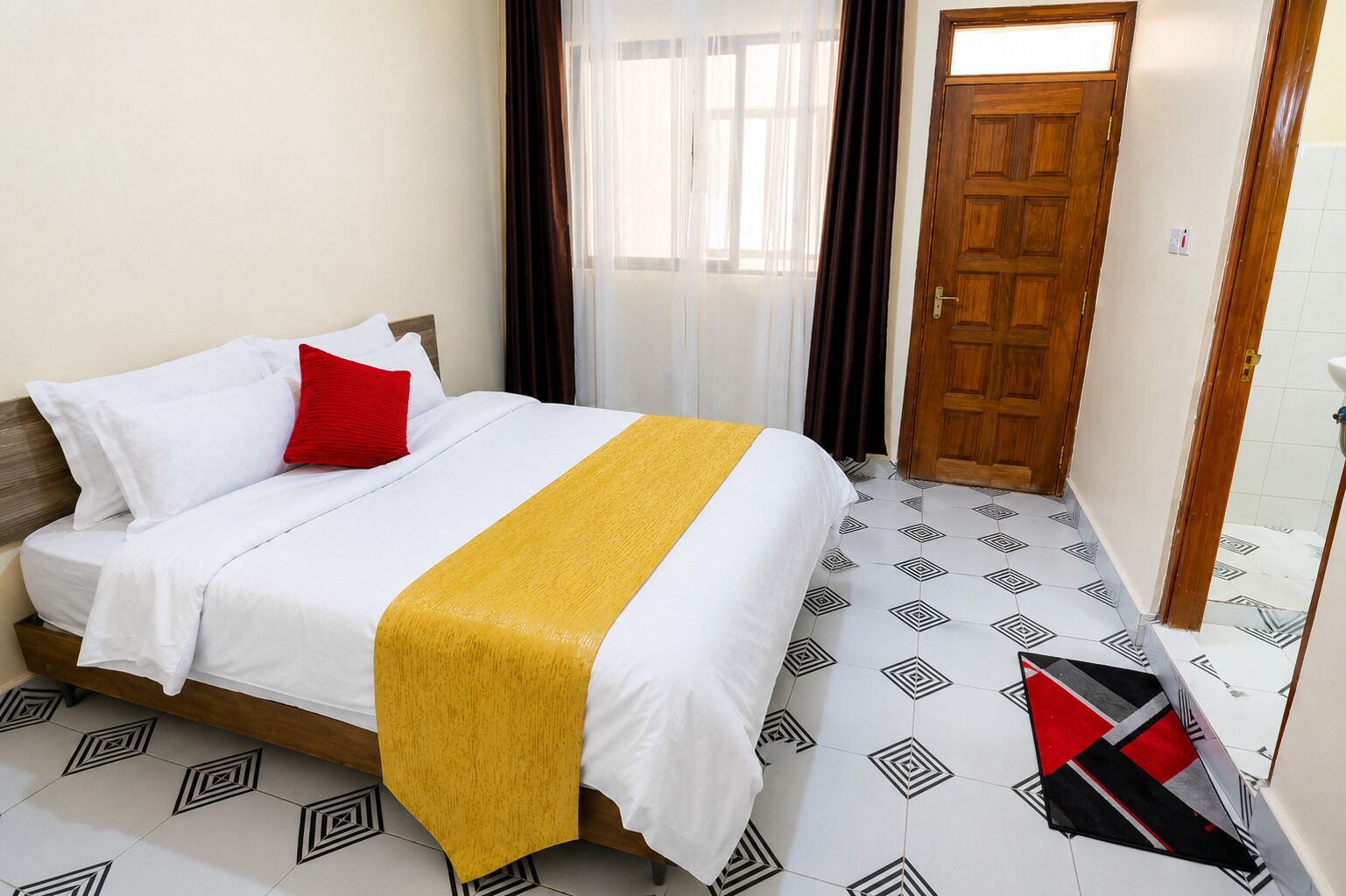 A hotel room with a bed, a wooden door, and patterned floor tiles.