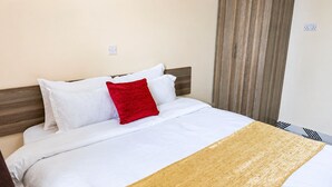 Una cama bien hecha con ropa blanca, una almohada decorativa roja y una manta color beige.