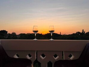 Dos copas de vino en un balcón con vista al atardecer.