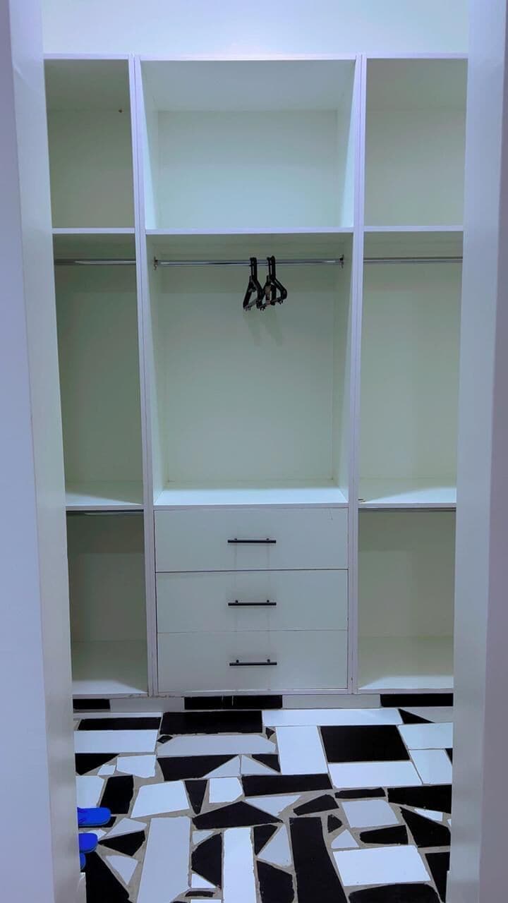 Un armario blanco con varios estantes y cajones, una barra para colgar ropa y un piso estampado.