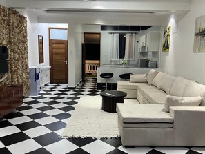 Una sala de estar con piso a cuadros, un sofá, una mesa de centro y una cocina al fondo.